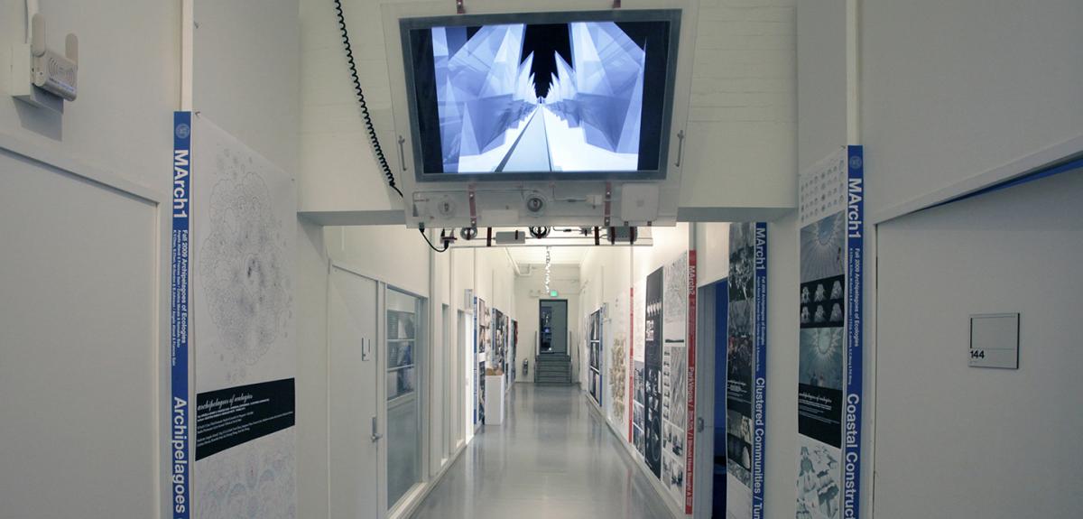 view of a white hallway with posters hung on both sides and a monitor hanging from the ceiling