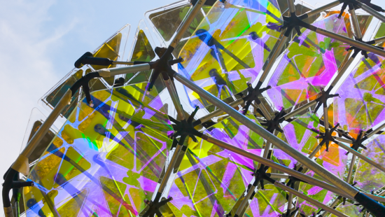 Holographic paneled metal structure outside with a bright blue sky.