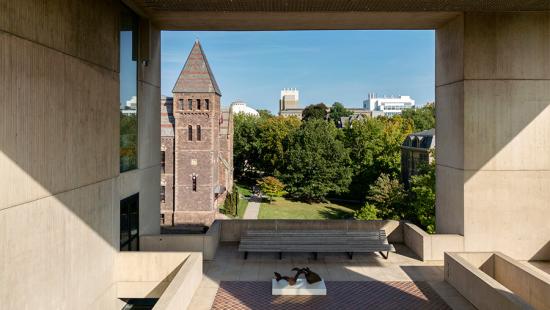 Large building framing a brick clock tower on a sunny day on a college campus