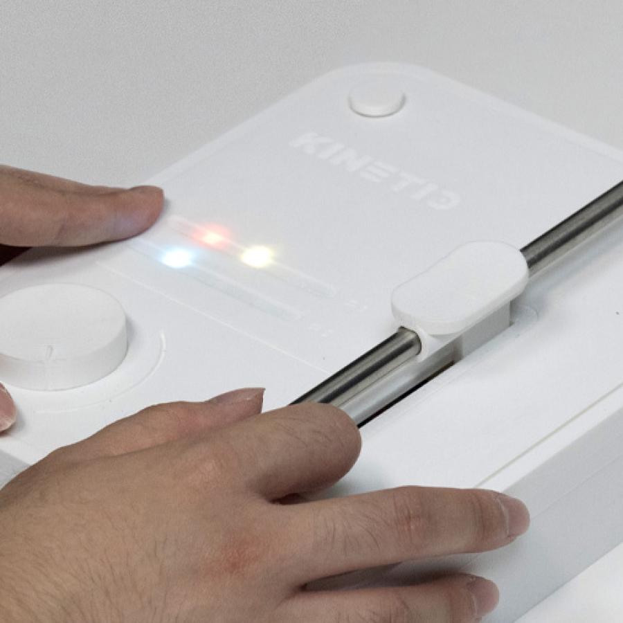 Two hands operating a white box-shaped device with diferent colored LED lights, an rotating knob, and a metallic rod.