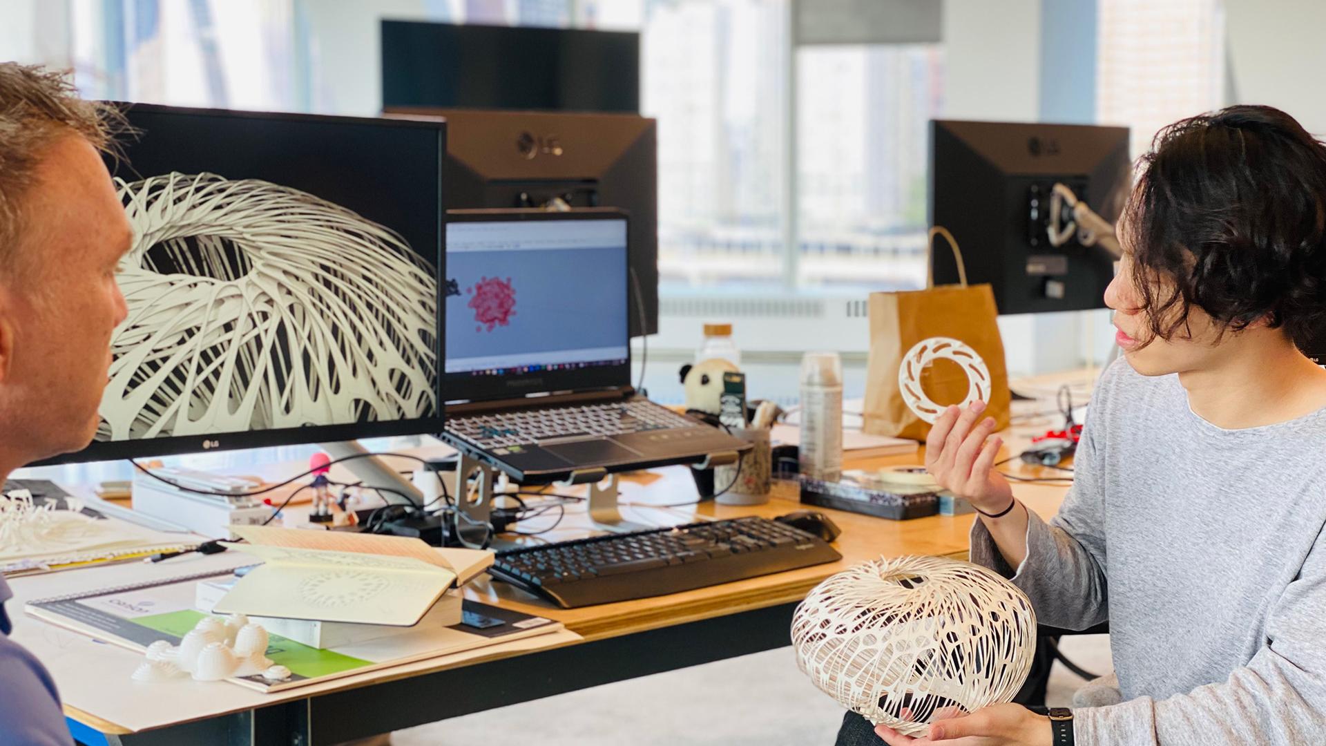 Two people sitting at a desk observing architectural models.