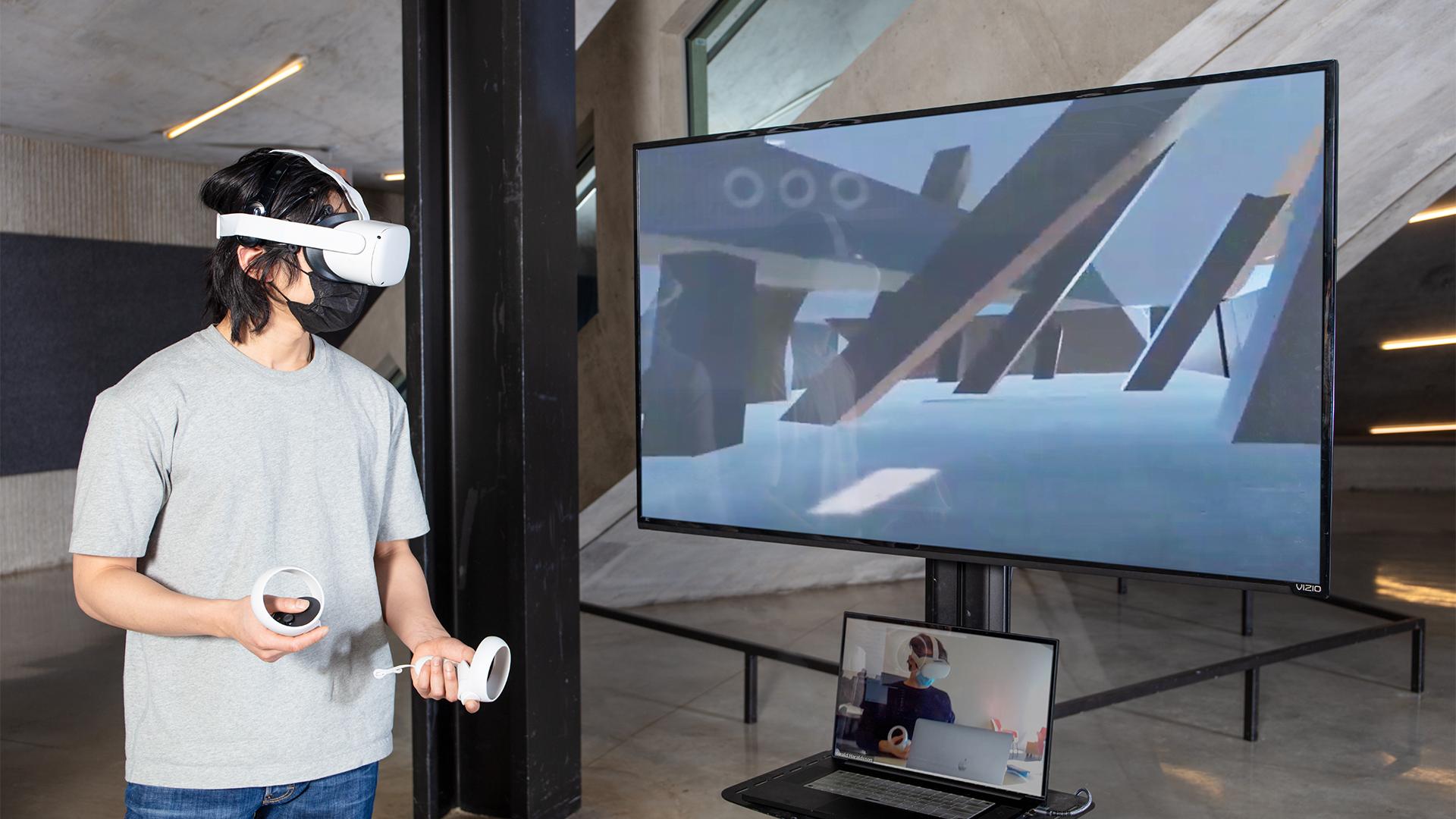 A person wearing a virtual reality headset and holding controllers in their hands with a screen in front of them.